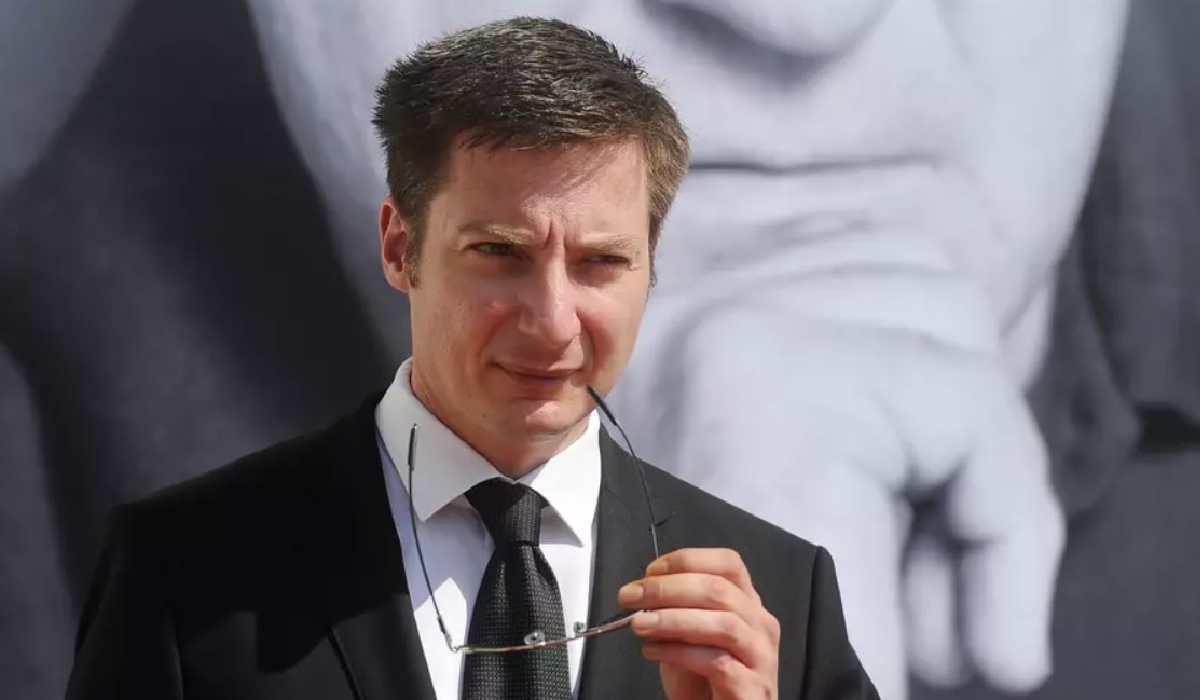 Andrei Caramitru, îmbrăcat într-un costum negru. Ține ochelarii într-o mână