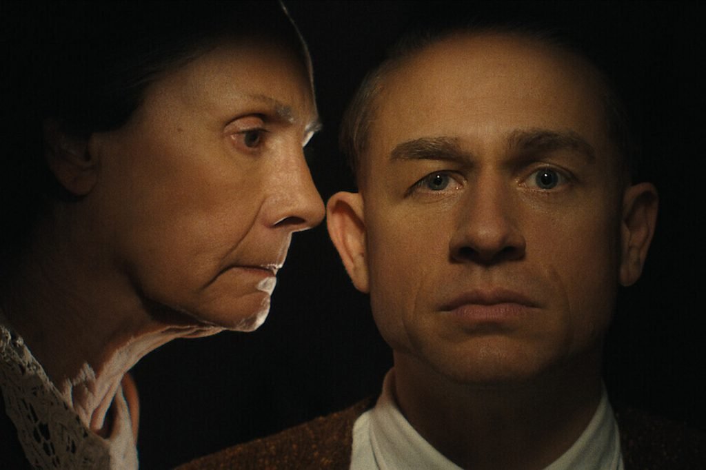 A cinematic image of an older woman on the verge of whispering something into a younger man's ear.