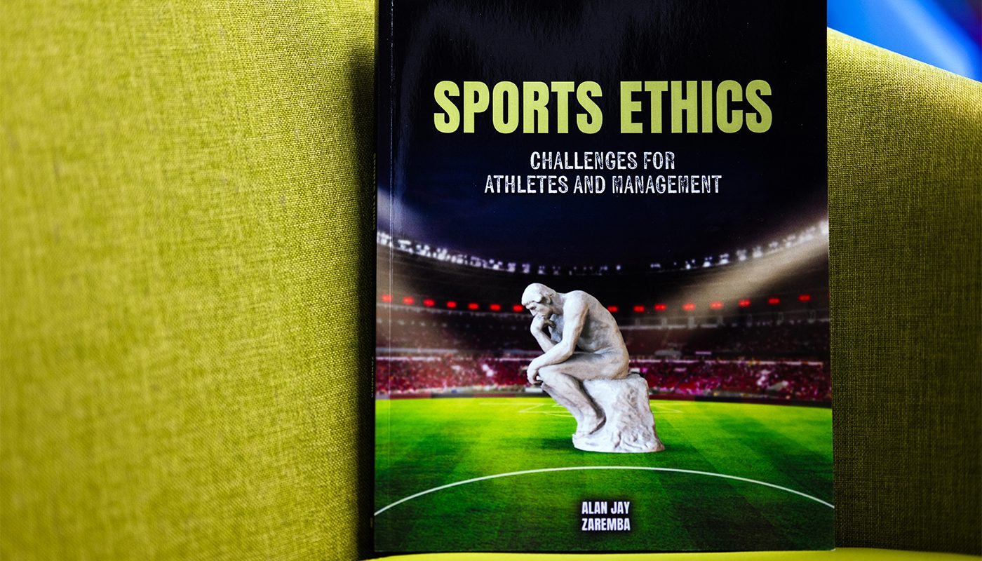 The cover of Sports Ethics, by Alan Zaremba. The book has a picture of Rodin's sculpture "The Thinker" on a stadium field. The book itself rests on a yellow couch.